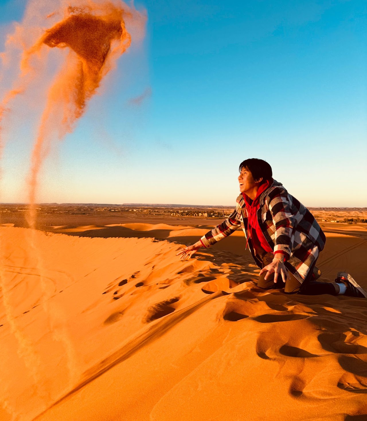 Wesley Lin kneeling on desert dunes with sand flying through the air